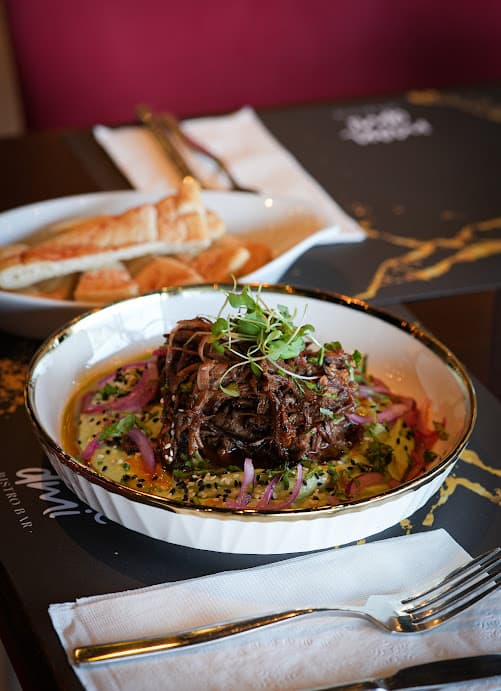 Short ribs en cocción lenta sobre hummus de aguacate, con pan pita al fondo